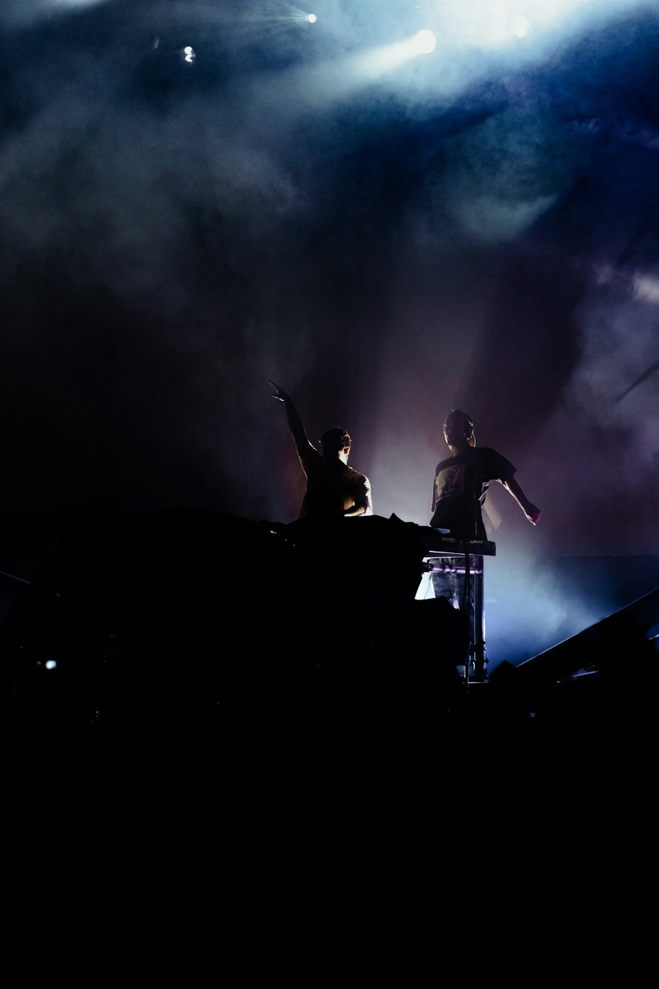 Two DJs perform music on a stage with sound equipment.