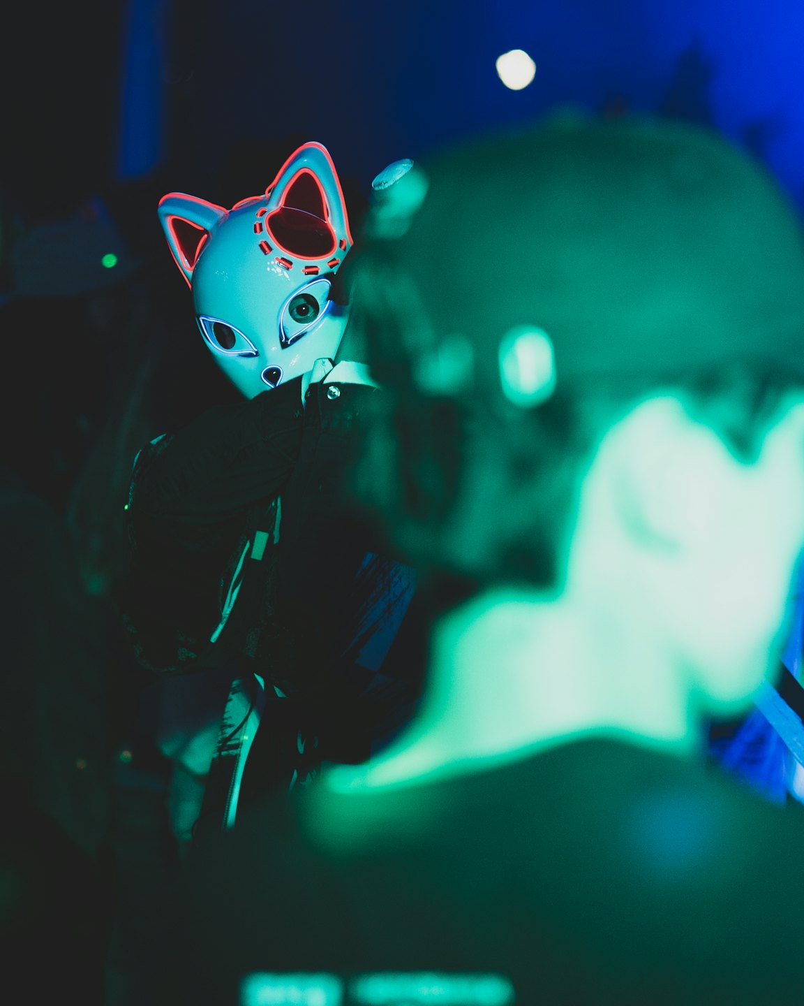 Person wearing a stylized white cat mask with neon accents.
