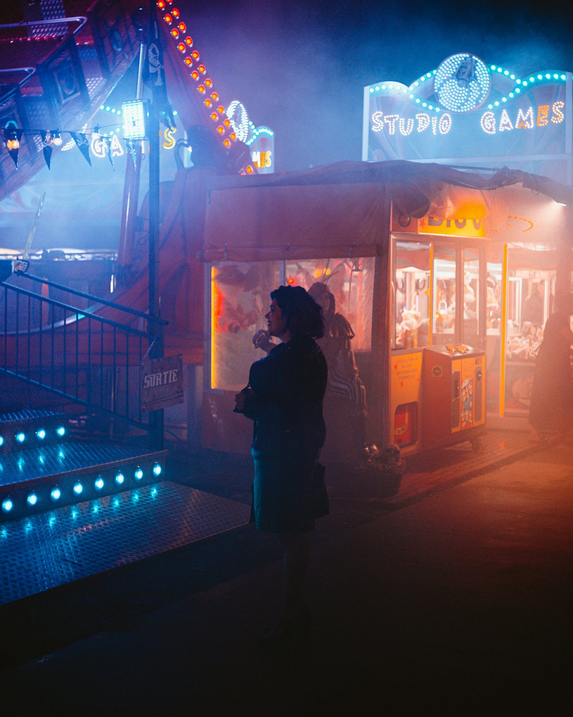 A person stands watching neon games at an amusement park.